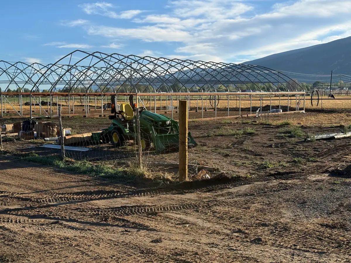 The metal frame of a new greenhouse going up, with a tractor and mountains in the background